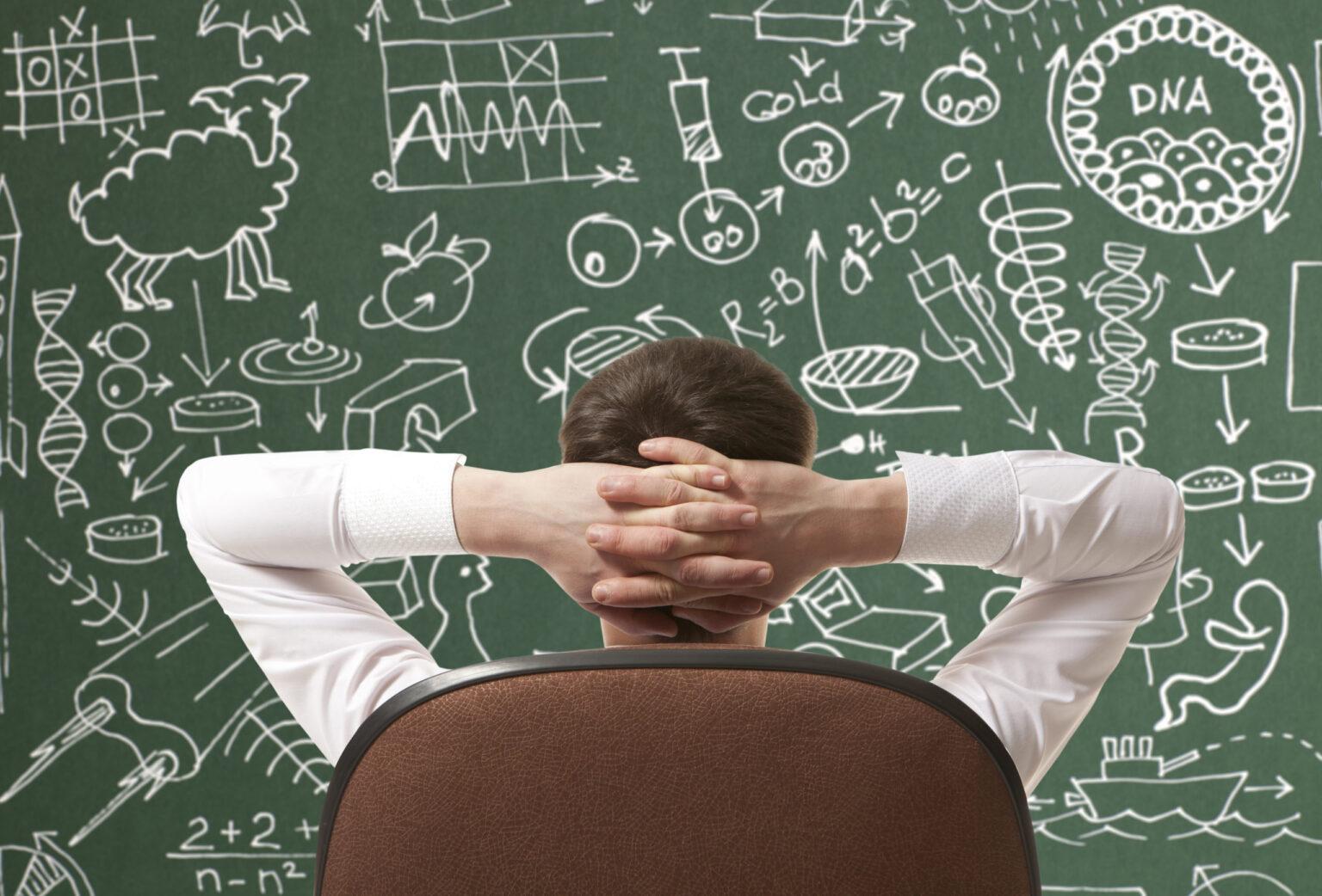 Inventors: Learn to Think Like an Examiner. Sign up today, Friday! 1 Rear view of man sitting an office chair, with hands behind head, facing a busy blackboard.